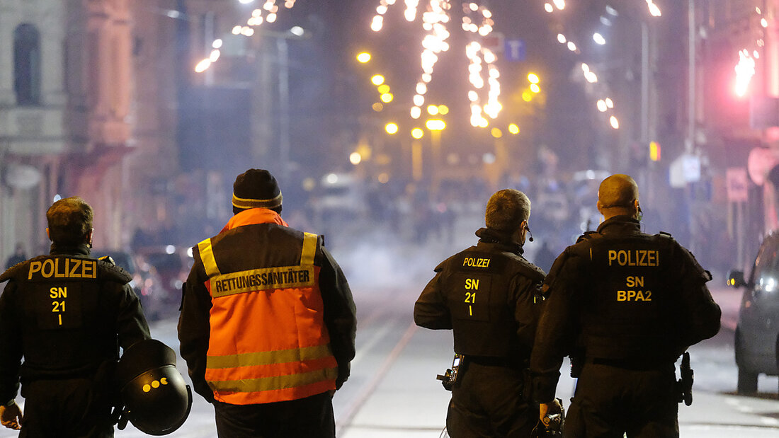 Polizisten und ein Rettungssanitäter stehen an einer Kreuzung. Die Stadt Leipzig hatte für die Silvesternacht Versammlungen verboten und in drei Zonen - darunter am Connewitzer Kreuz - ein Böllerverbot erlassen. Foto: Sebastian Willnow/dpa-Zentralbild/dpa 20210101102740486.jpg