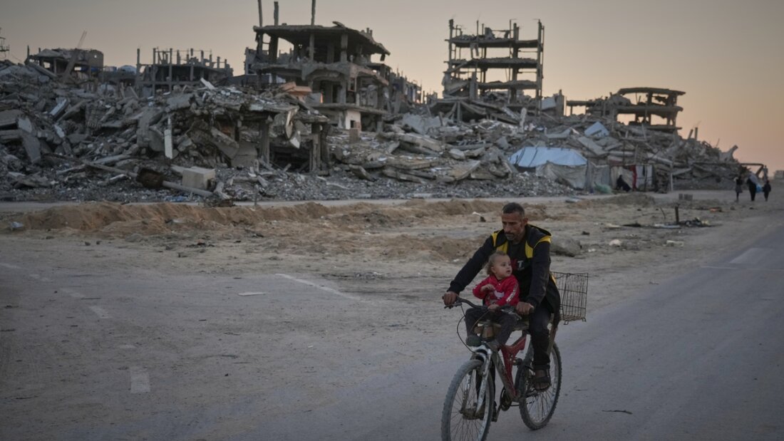 dpatopbilder - Ein Mann trägt ein Kind, während er mit dem Fahrrad eine beschädigte Straße im Lager Al-Shati entlangfährt. Foto: Jehad Alshrafi/AP/dpa 20251119070537651.jpg