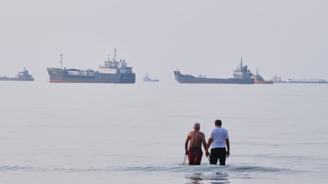 Zwei Männer waten durch das Wasser der Straße von Hormus, während im Hintergrund Schiffe vor Anker liegen. Foto: Razieh Poudat/ISNA via AP/dpa 20260714060117840.jpg