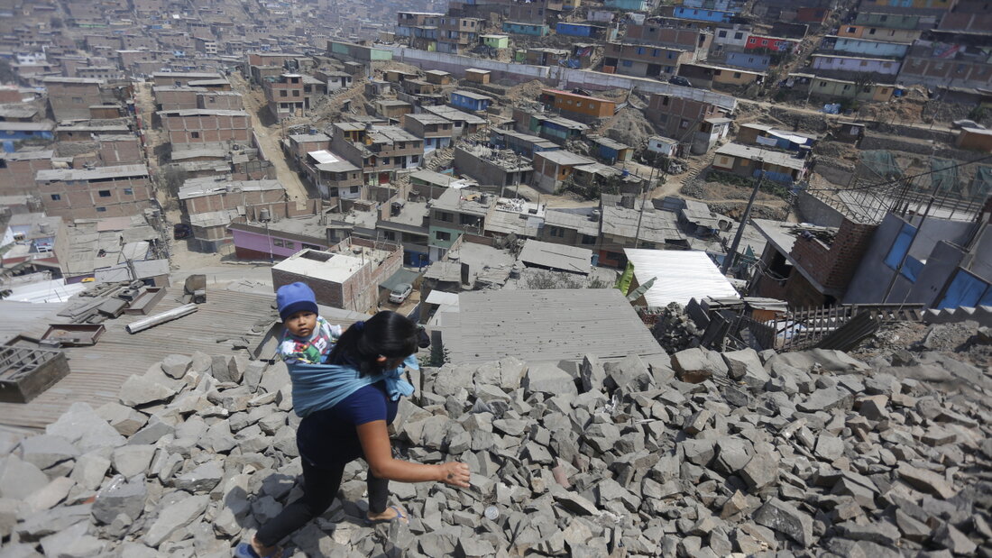 ARCHIV - Eine Frau trägt ihr Kind am Rücken und geht über Steine zu einem Haus in Lima, in dem Essen verteilt wird. Foto: Gian Masko/dpa 20260820214930068.jpg