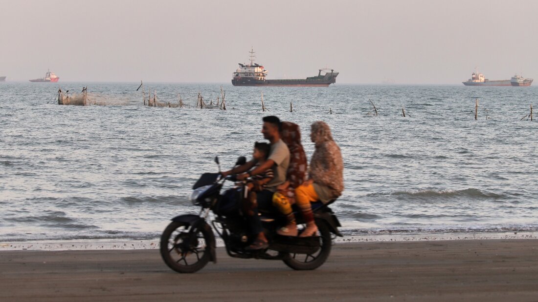 ARCHIV - Fracht- und Serviceschiffe säumen den Horizont, während Menschen auf einem Motorrad über den Strand am Ufer der Straße von Hormus fahren. Foto: Amirhosein Khorgooi/ISNA/dpa/Symbolbild 20260712193256614.jpg