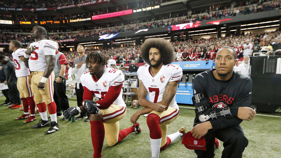Colin Kaepernick (Mitte), damals Quarterback der San Francisco 49ers, kniet am 18. Dezember 2016 vor der NFL-Partie gegen die Atlanta Falcons während der Nationalhymne nieder 20260901113244846.jpg