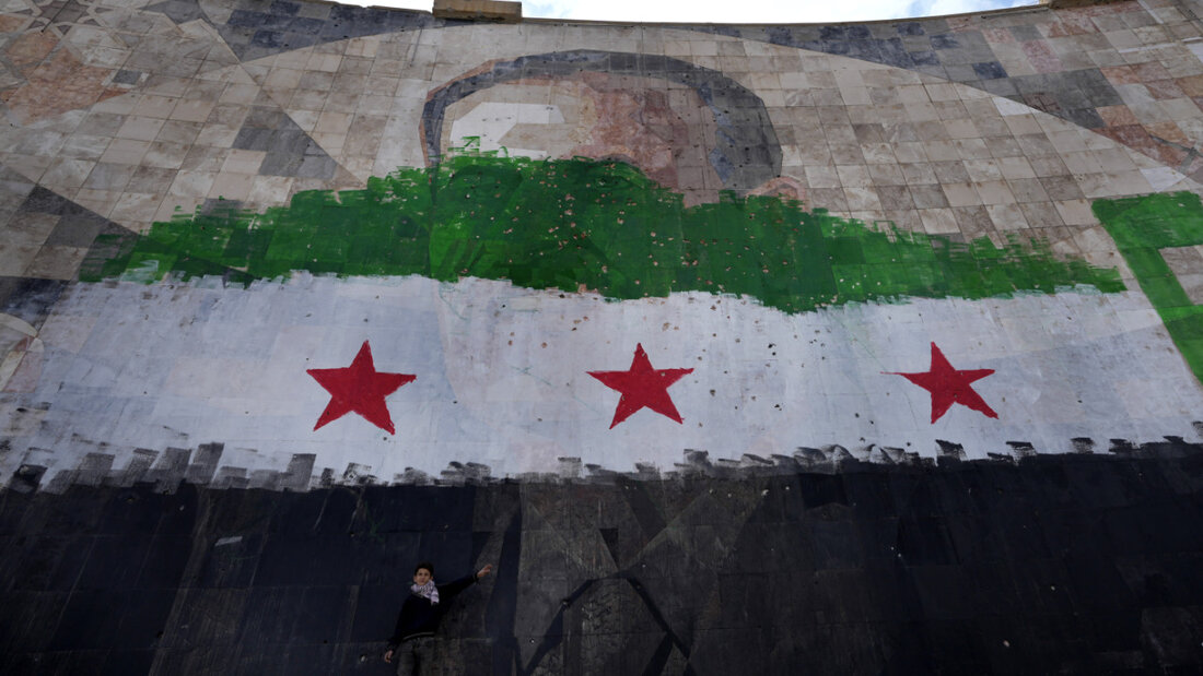 ARCHIV - Ein syrischer Junge steht unter einem riesigen Porträt des verstorbenen syrischen Präsidenten Al-Assad, übermalt mit den Farben der sogenannten "revolutionären" Flagge, in Damaskus. Foto: Hussein Malla/AP/dpa/Symbolbild 20251114221830241.jpg
