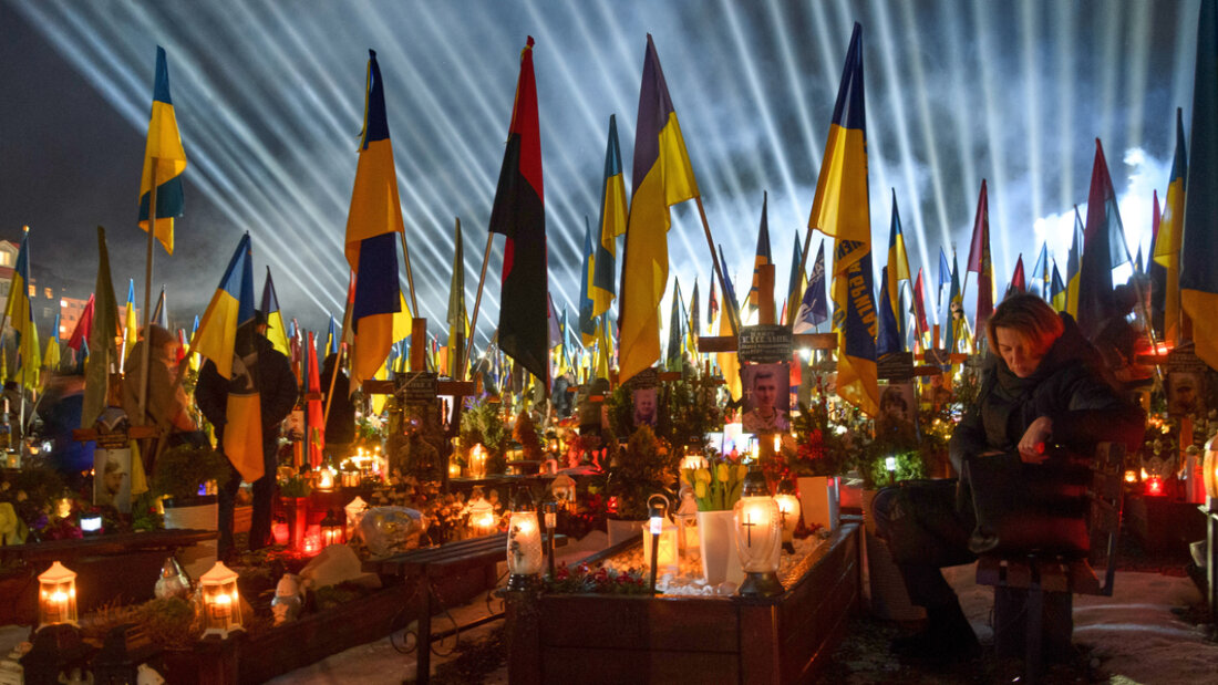 Flutlichter leuchten über den Gräbern der gefallenen Soldaten, während Menschen am Vorabend des vierten Jahrestages der russischen Invasion Kerzen anzünden. Foto: Mykola Tys/AP/dpa 20260224045732514.jpg